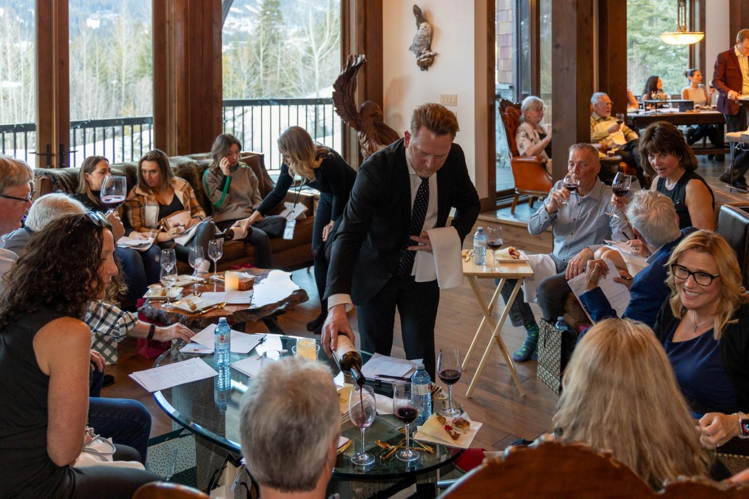 Gathering of people in a cozy room, waiter serving wine.