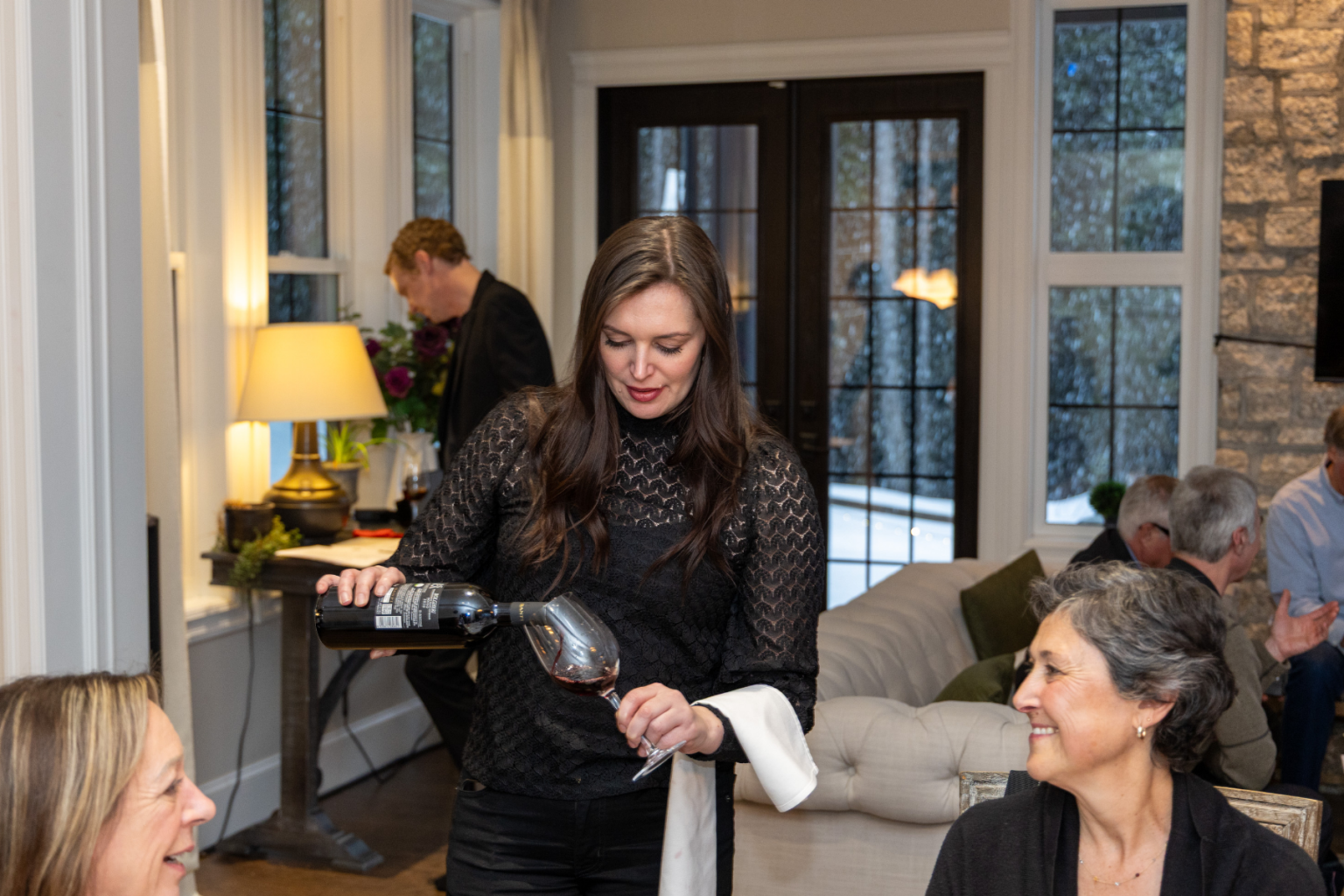 Woman pouring wine at a gathering in a cozy living room.