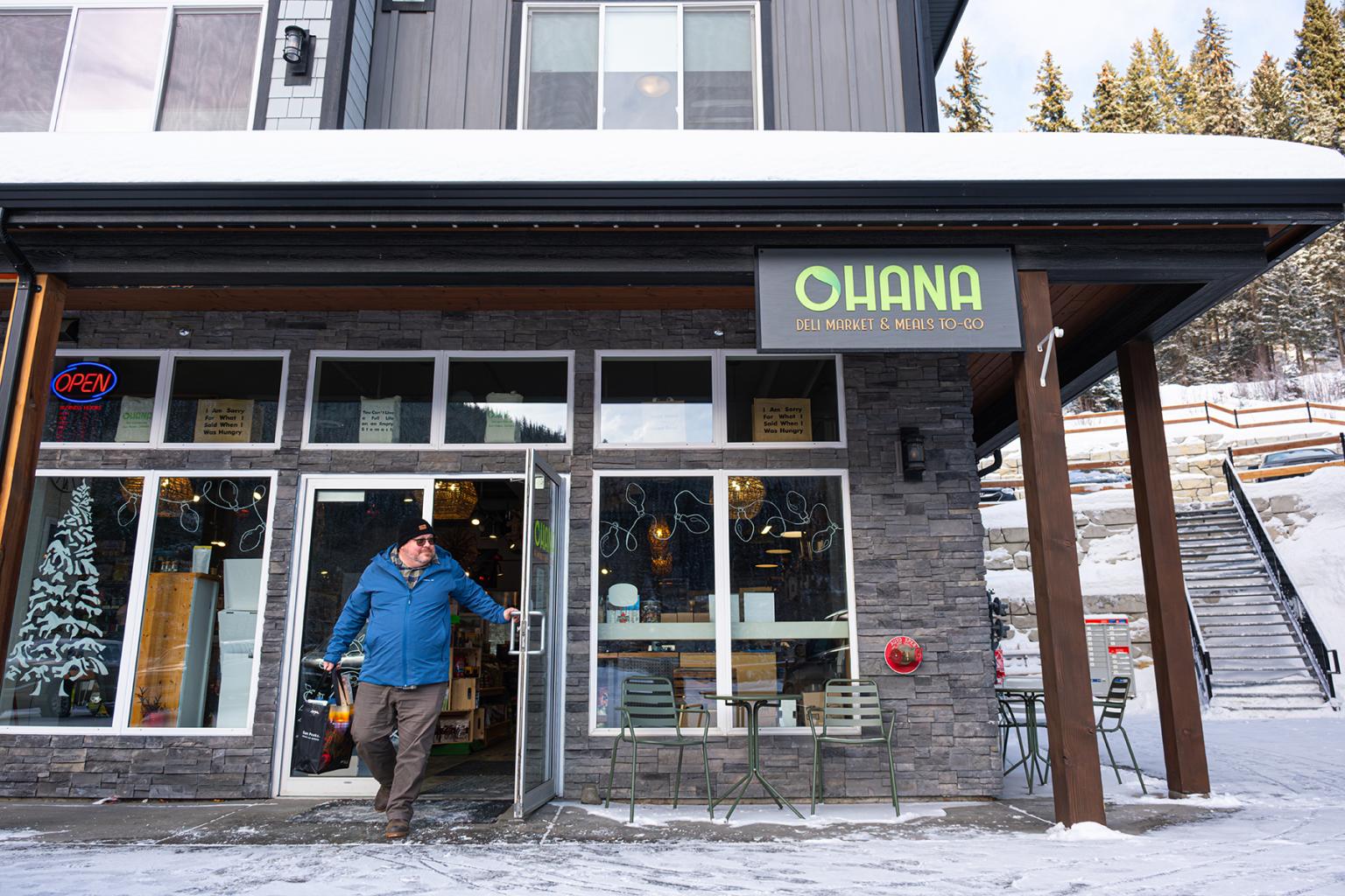 Man walking out the front door of Ohana Deli in Sun Peaks with bag of groceries