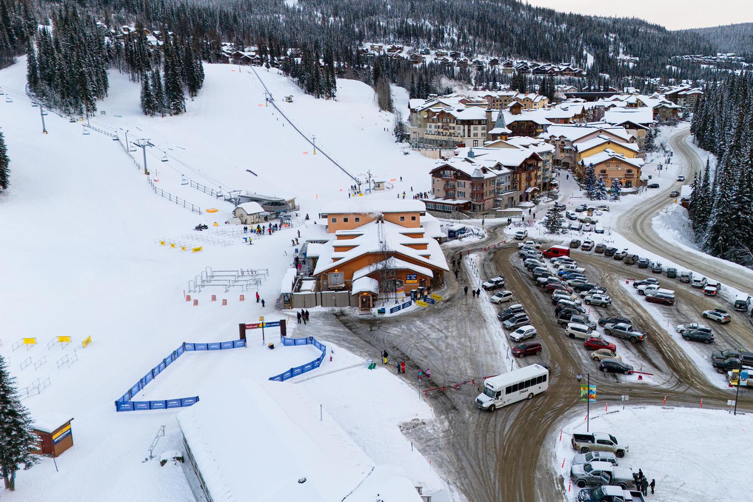 Aerial view of Sun Peaks Resort village day lodge parking lot and chairlift base area, with resort shuhttle stopped to let off passengers