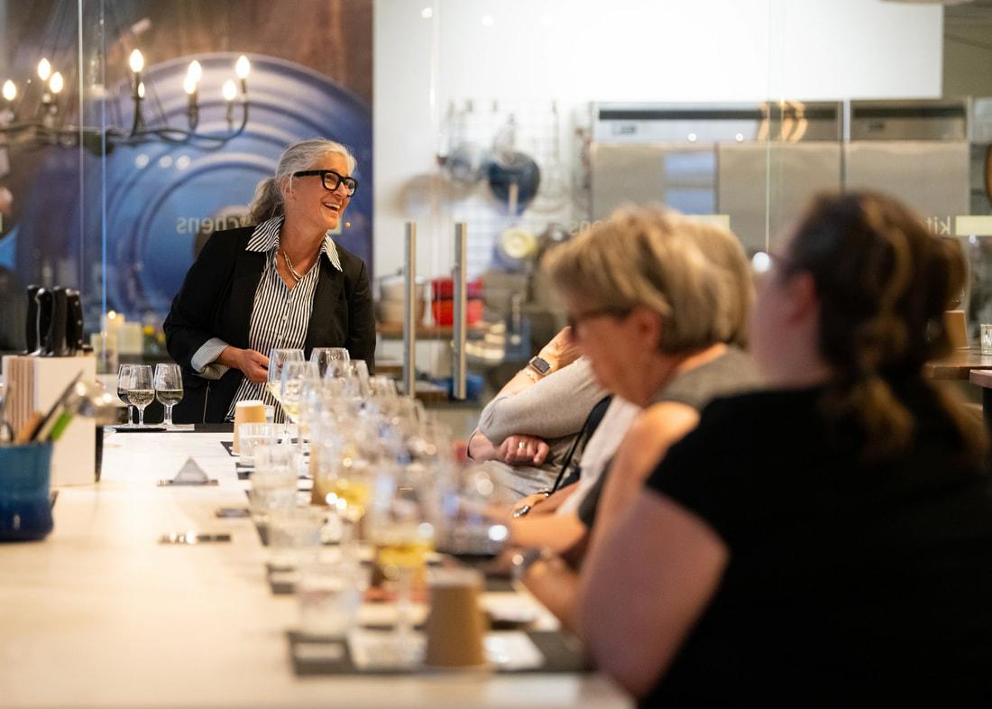 Group seated at a long table, woman standing and smiling at the head.