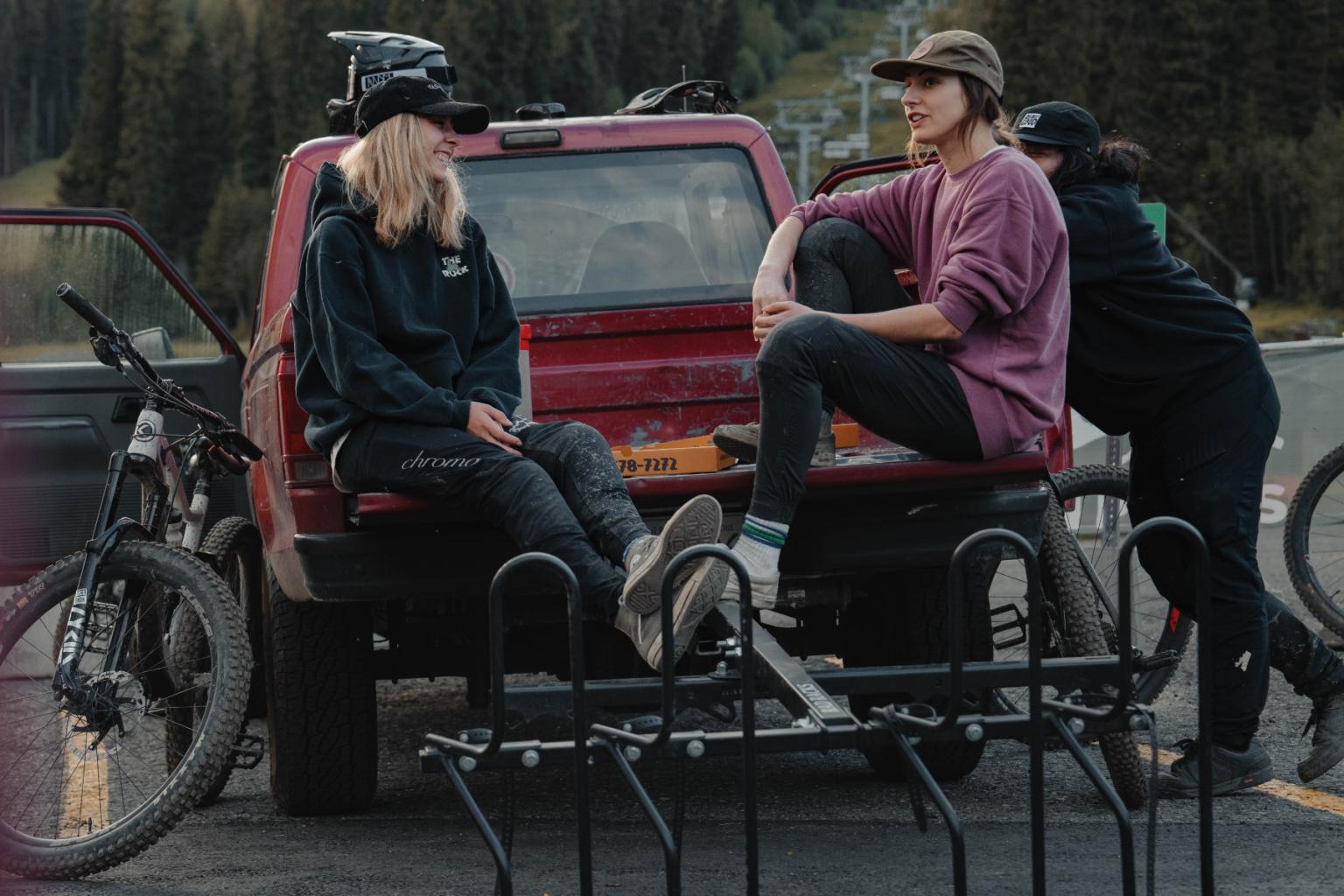 Two people sitting on a truck tailgate with parked bicycles nearby.