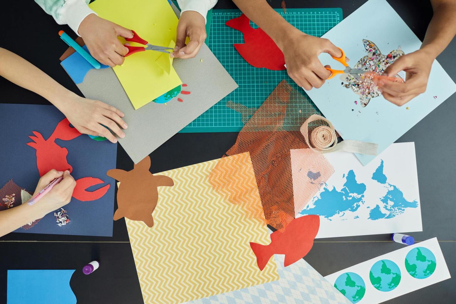 Hands crafting with colorful paper, scissors, and glue on a table.