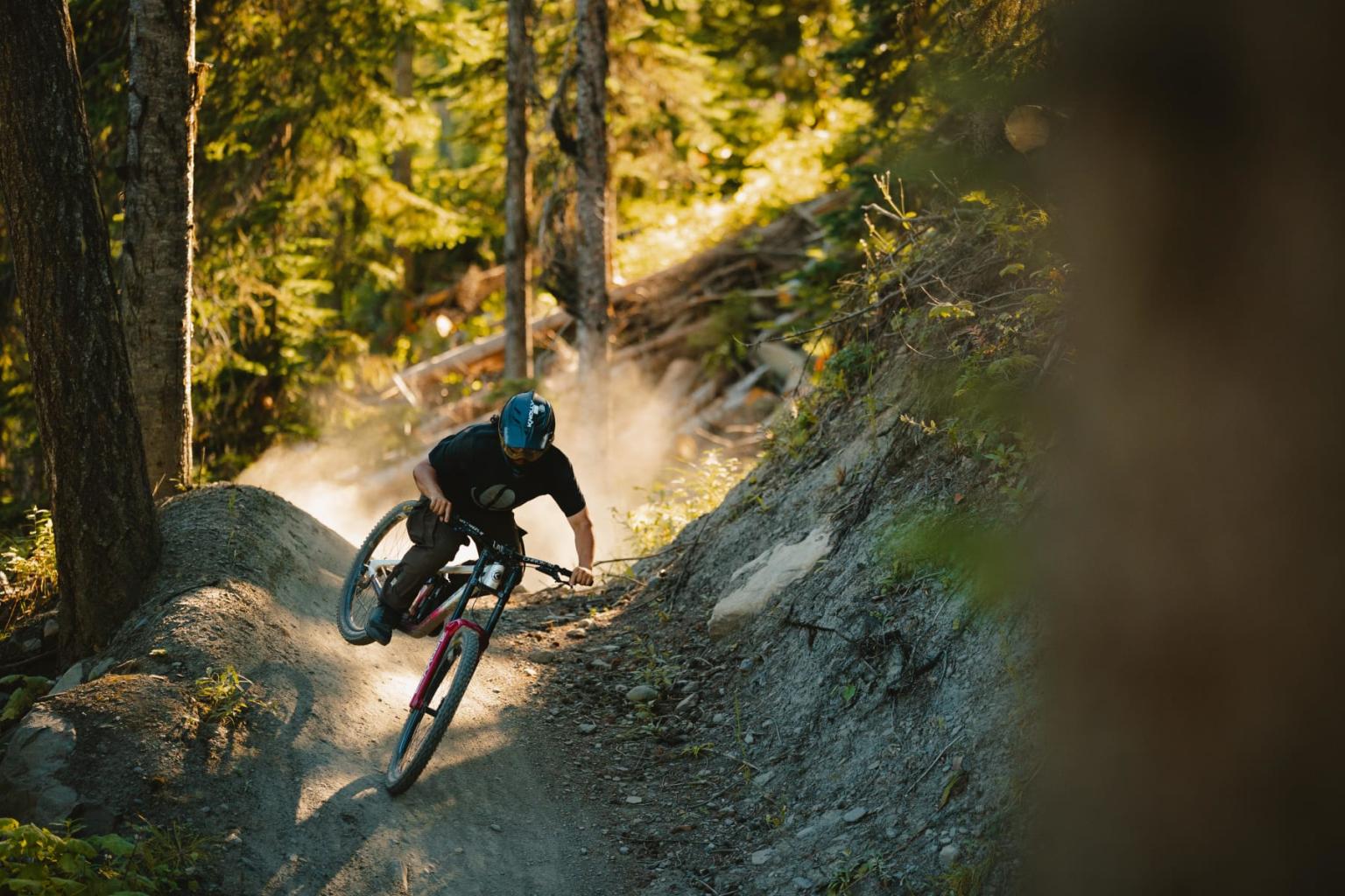 Mountain biker on a forest trail, kicking up dust in sunlight.