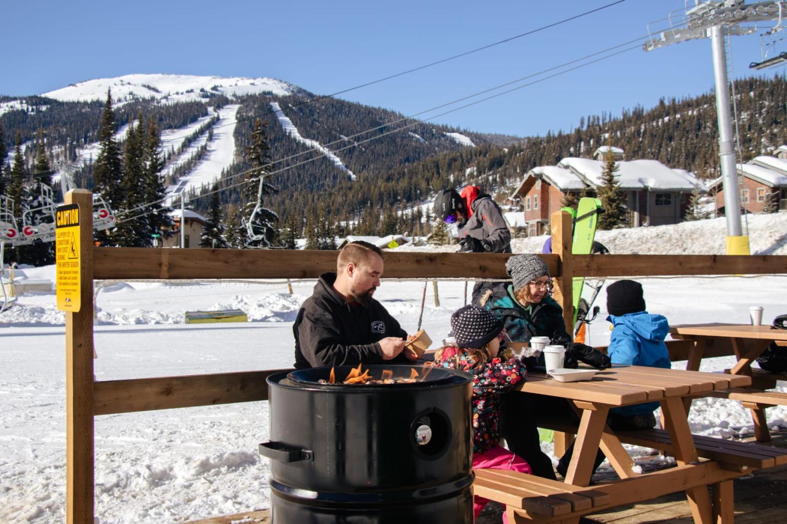 People sitting at a picnic table in a snowy mountain ski resort.