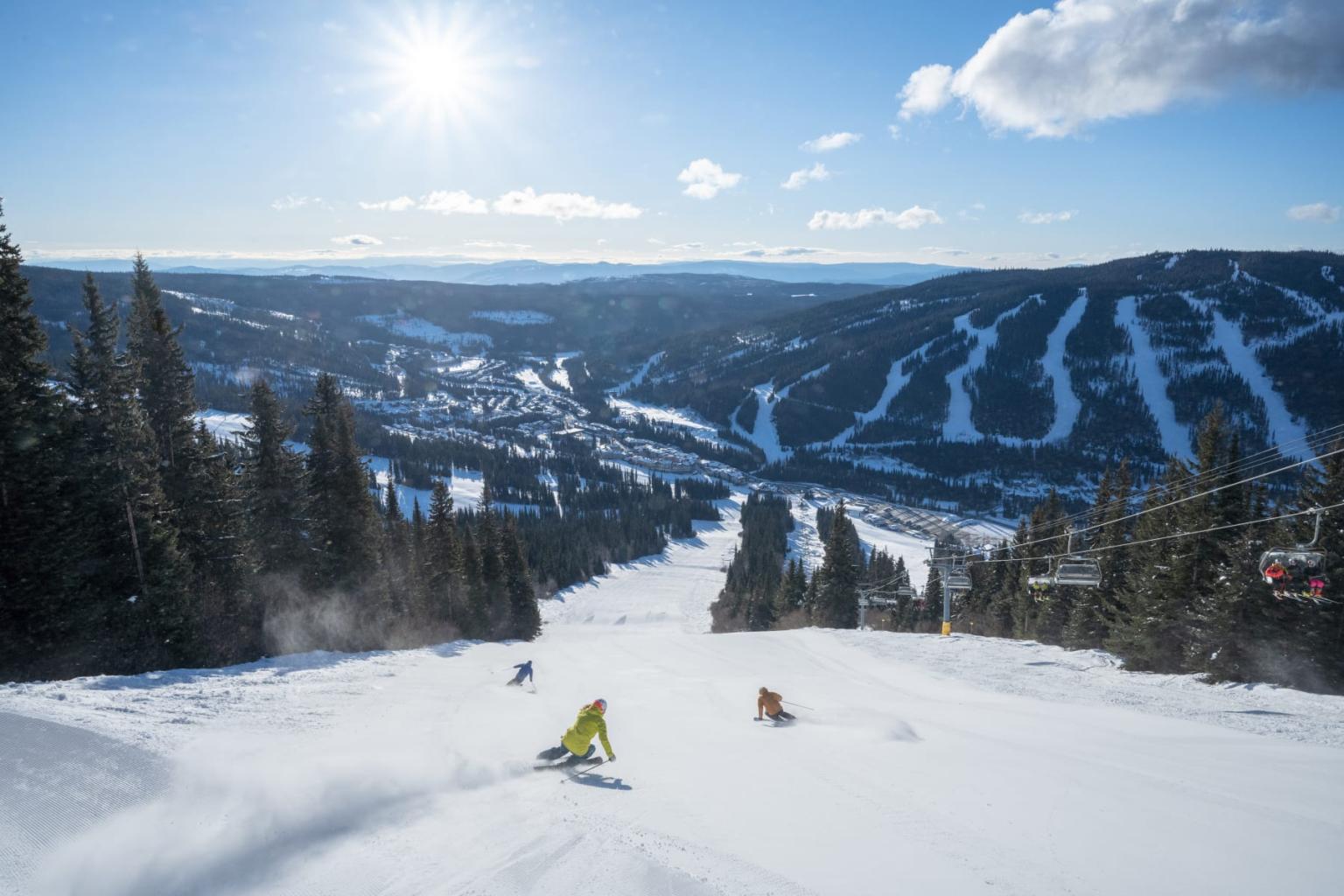 Skiers on a sunny snowy slope with distant mountain view.