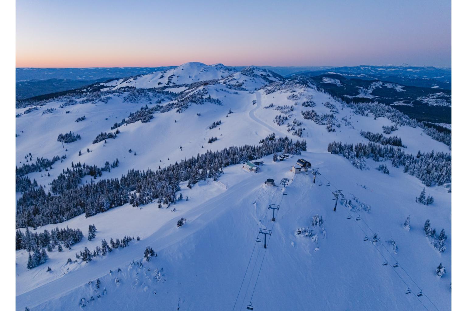 Snowy mountain landscape at dusk with ski lifts and trees.