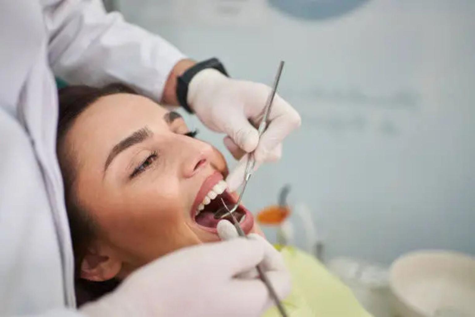 Dentist examining a patient's open mouth with tools.