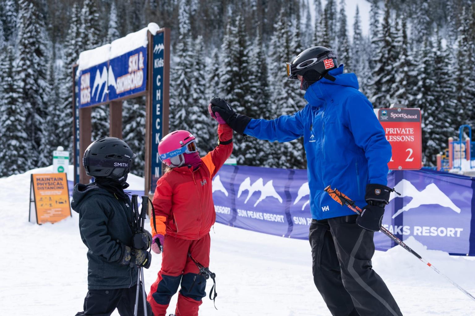 Child skiers high-fiving an instructor at a snowy ski resort.