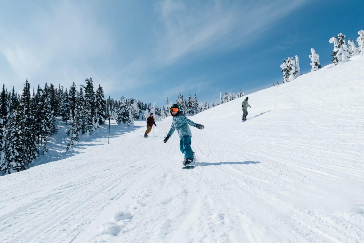 Snowboarders descending a snowy mountain under a clear blue sky.