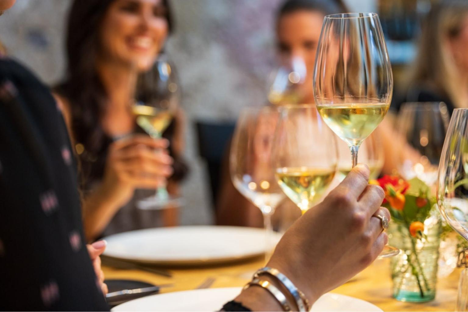 People toasting with white wine at a dining table.