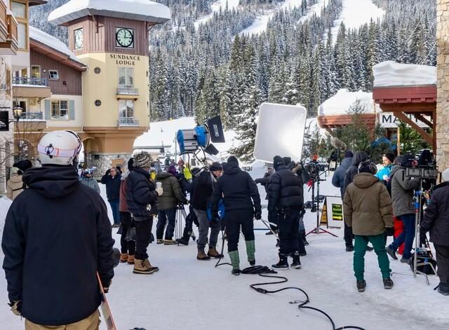 Film crew filming in a snowy village with buildings and trees.