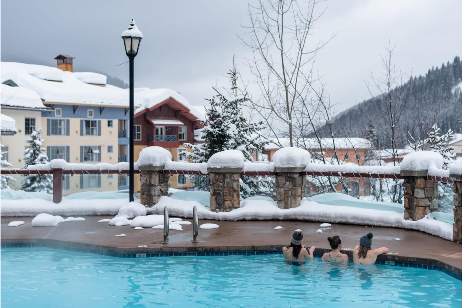 Outdoor hot tub in a snowy mountain resort with three people relaxing.