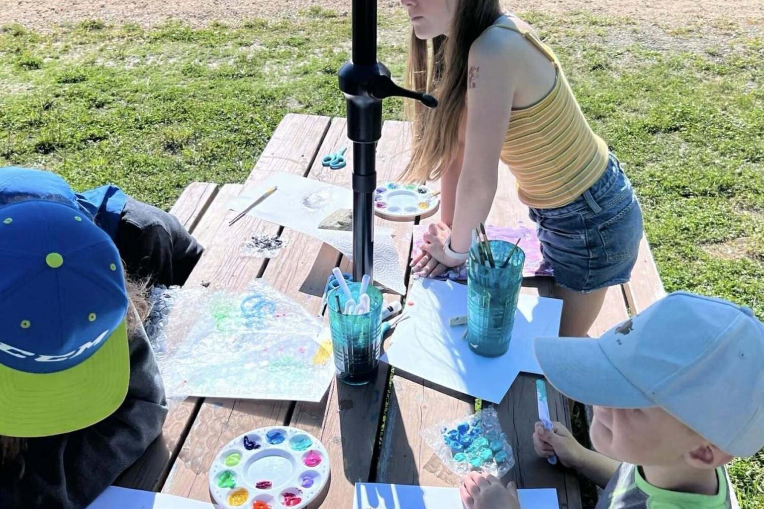 Outdoor painting activity at a picnic table with children and art supplies.