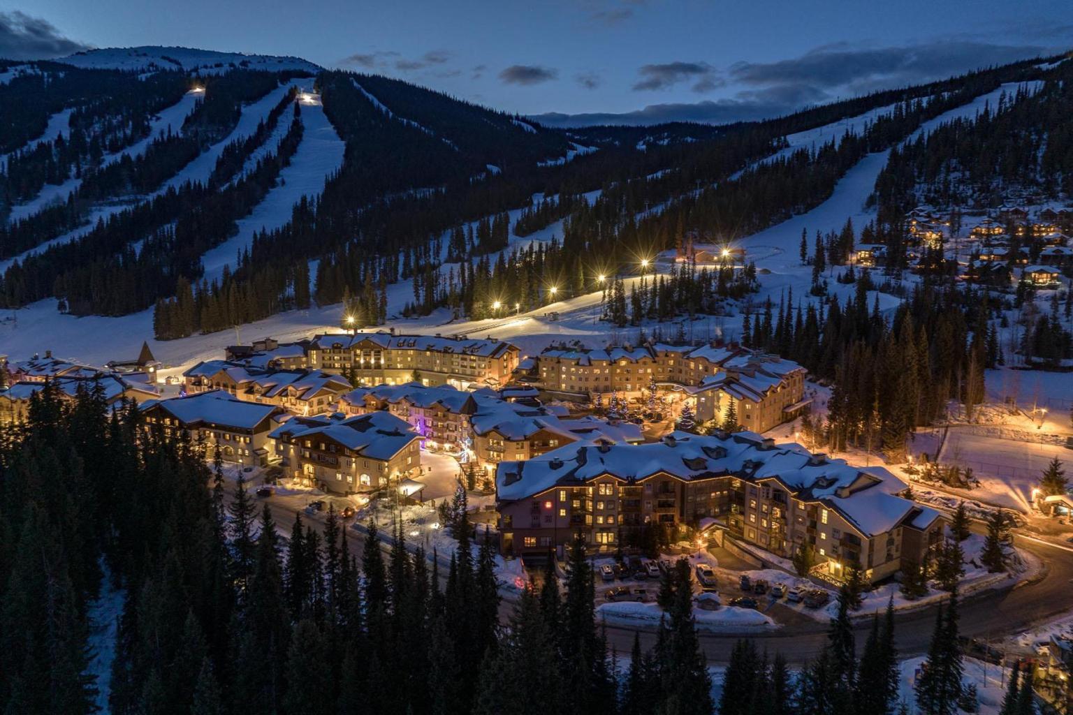 Snowy mountain village at dusk, with warm glowing lights and ski slopes.