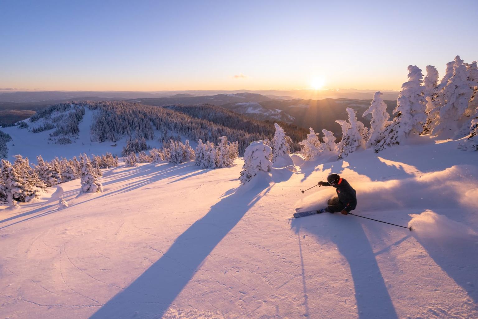 Skier on snowy slope at sunrise, casting long shadows.