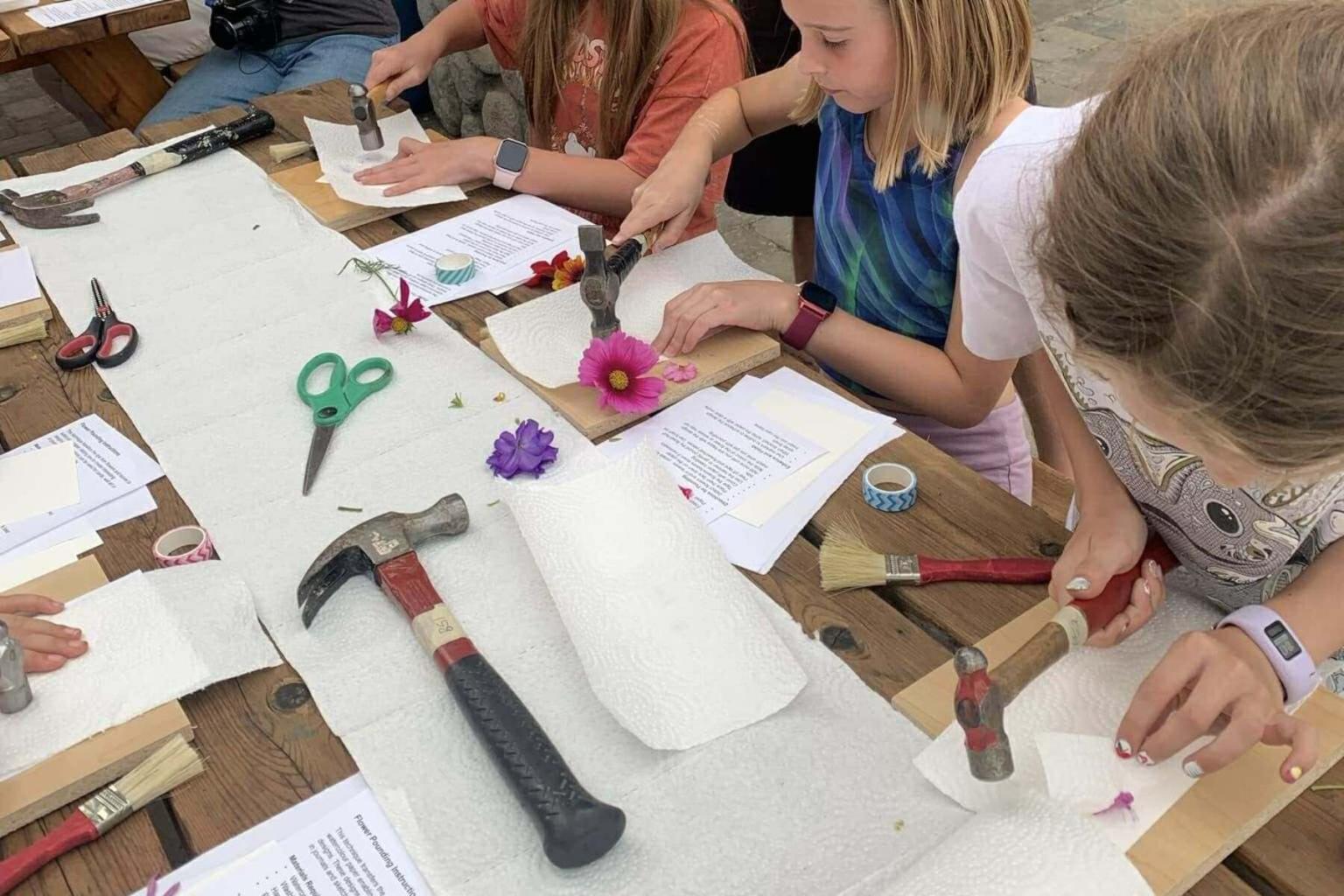 Kids hammer flowers onto paper at a crafting table.