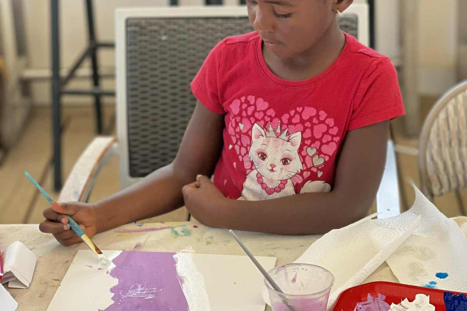 Child painting on paper with purple paint, wearing a red cat shirt.