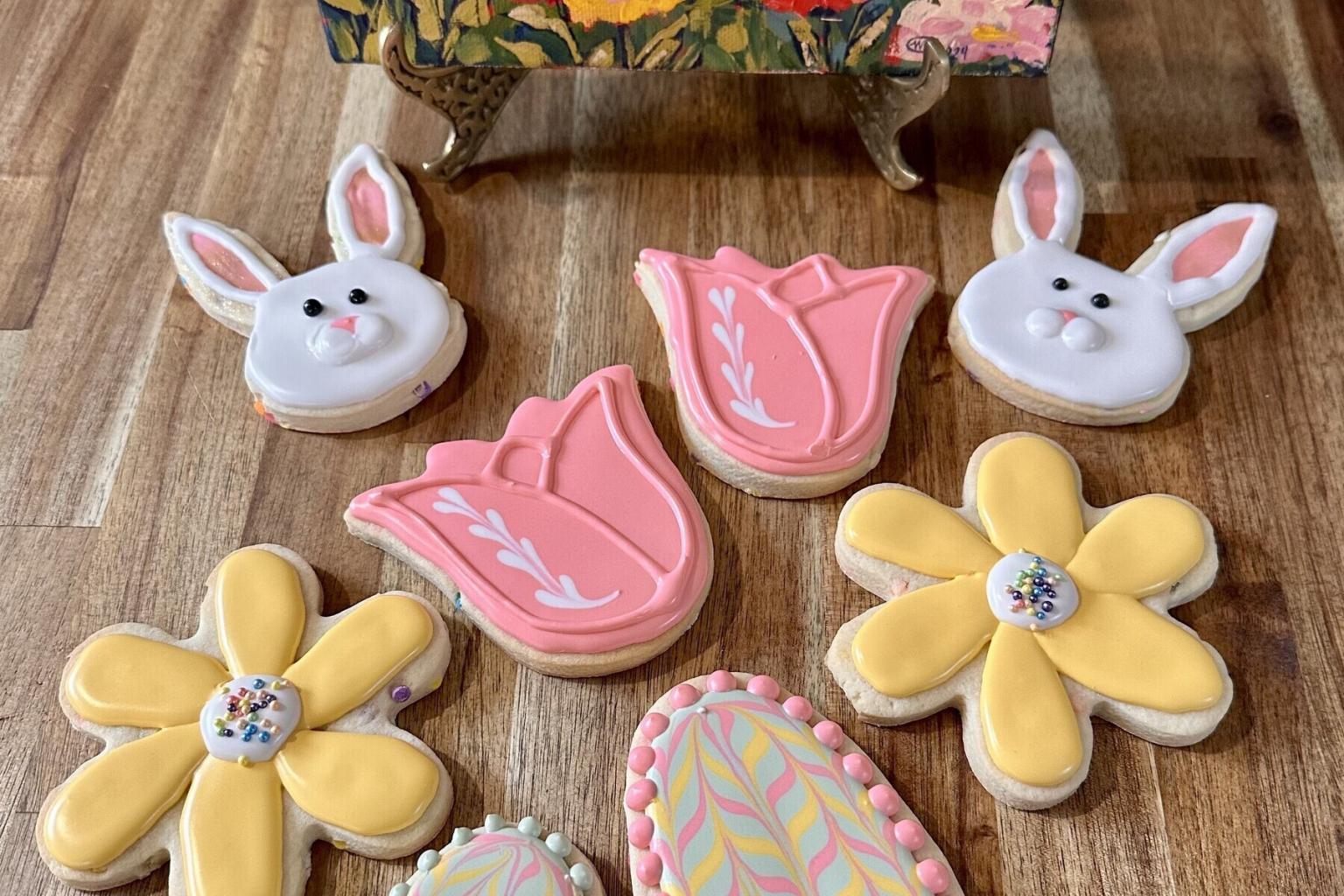 Decorative cookies shaped like bunnies, tulips, and daisies on a wooden surface.