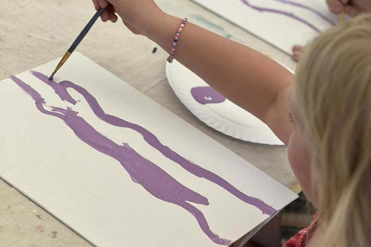 Child painting with purple paint on paper.