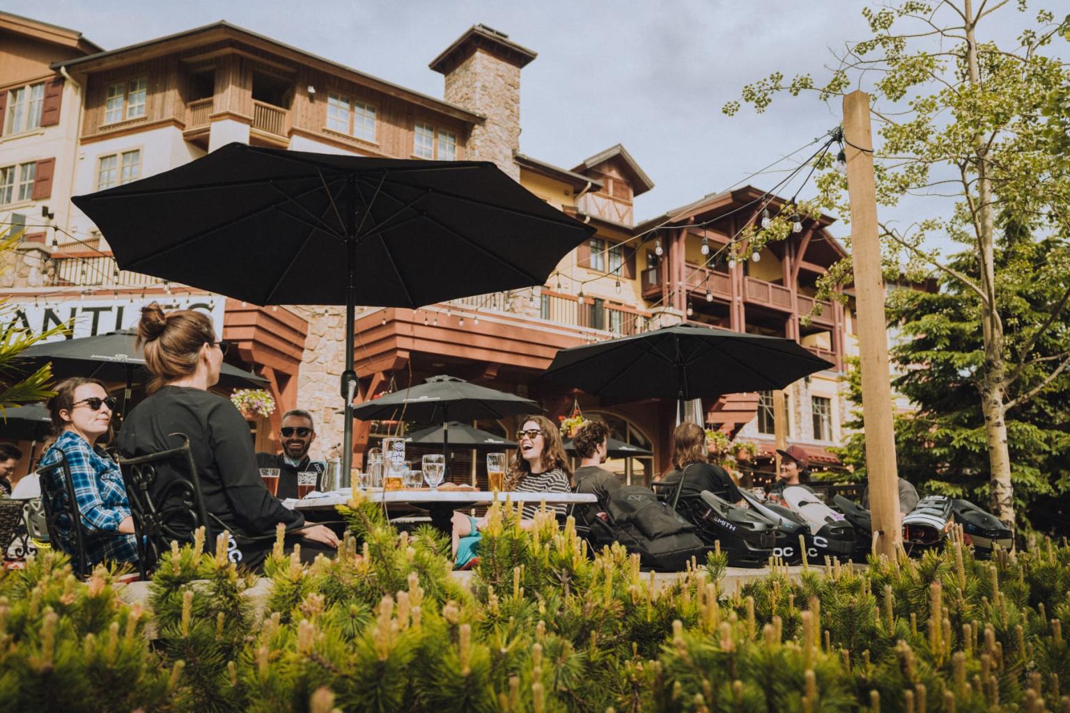Outdoor dining with people at tables, under large black umbrellas, near a rustic building.