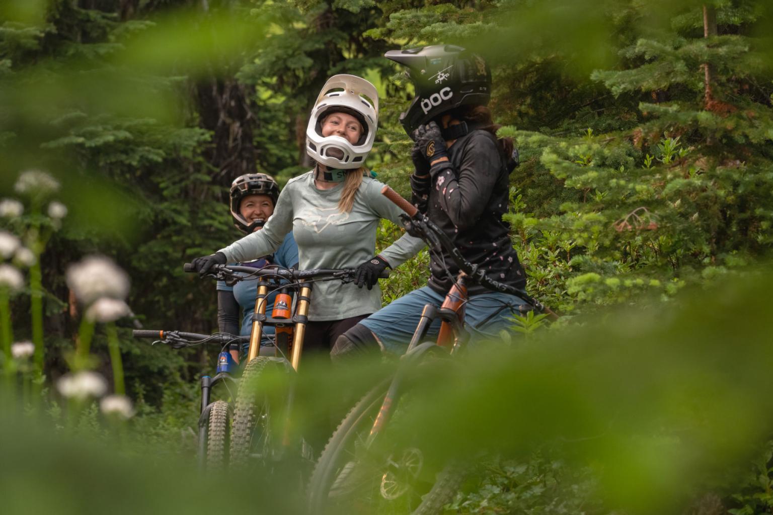 Bicyclists wearing helmets laughing in a forest setting.