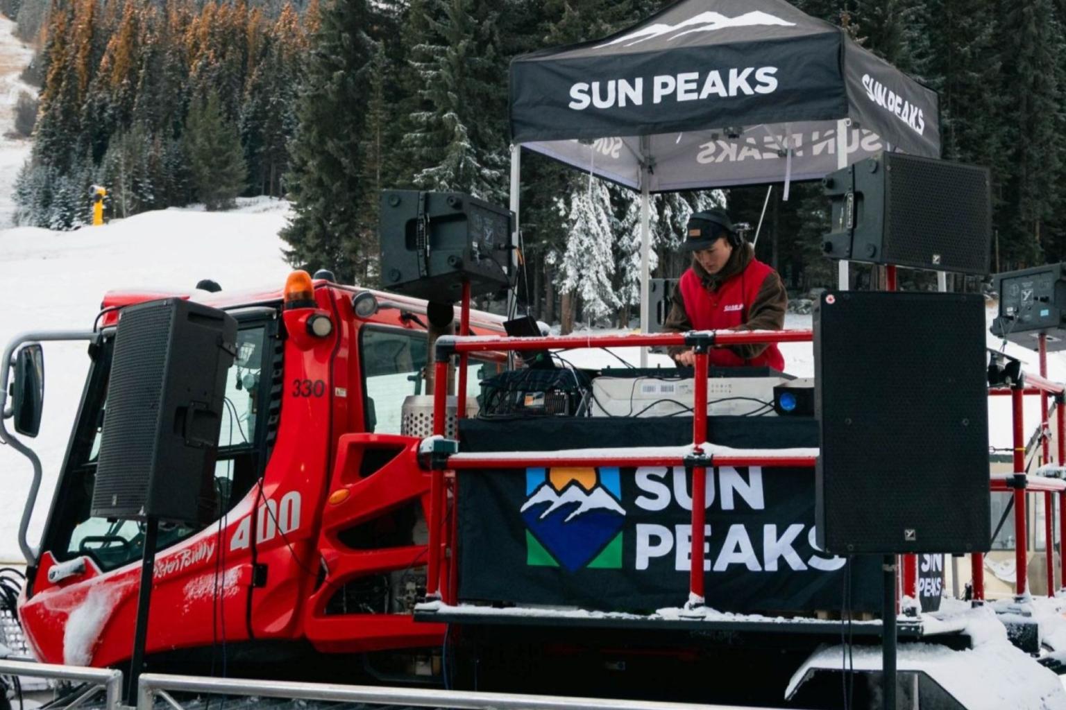 Red snowplow with DJ booth and "Sun Peaks" branding on a snowy day.