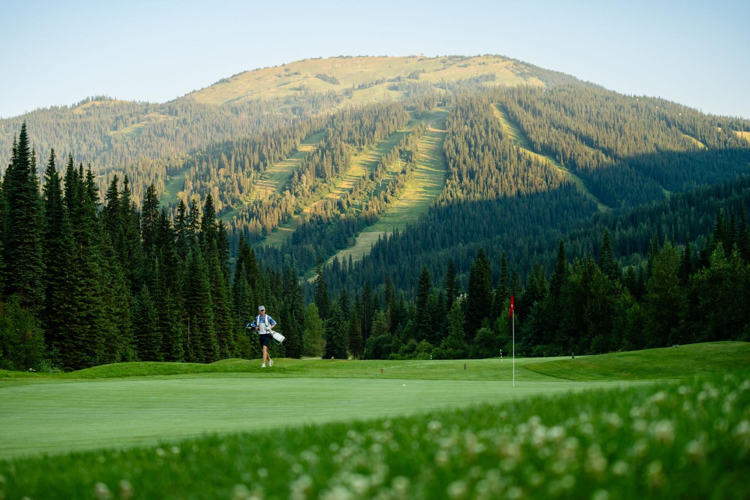 Golf course with distant player and mountain view at sunset.