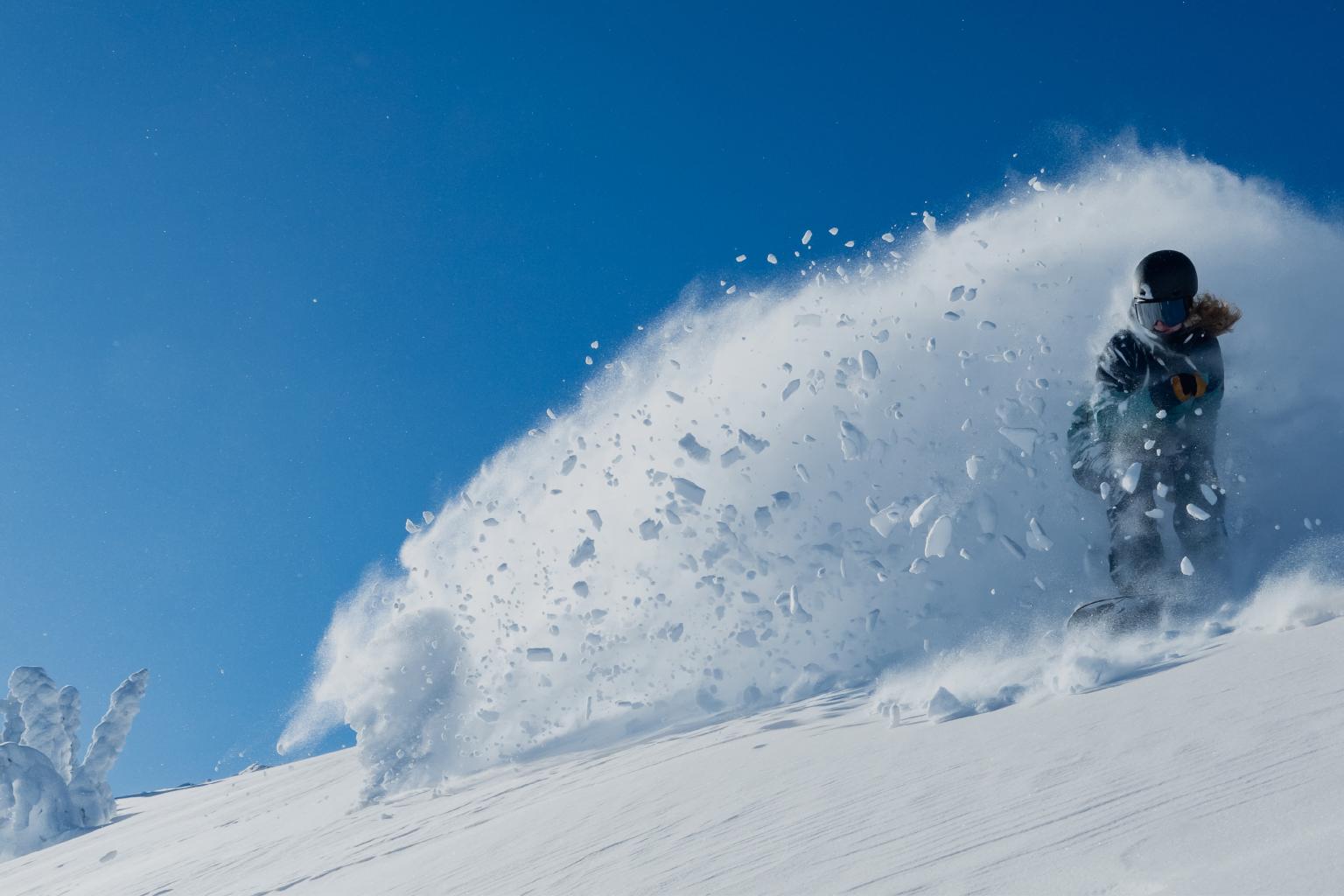 Snowboarder carving through snow, blue sky background.