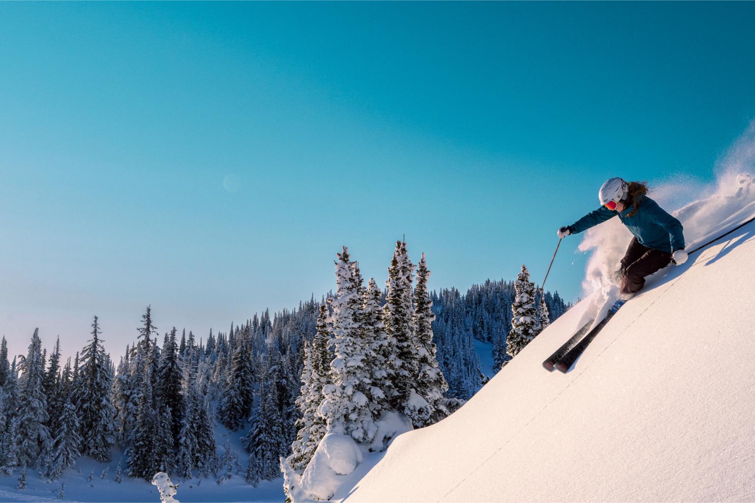 Skier descending snowy slope under clear blue sky.
