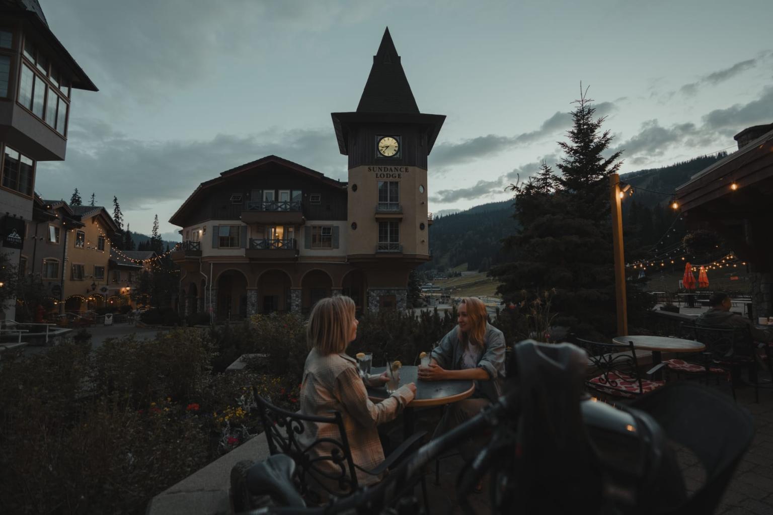 Couple dining outdoors at dusk near a clock tower in a village setting.