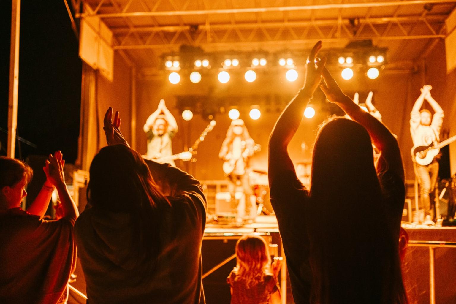 Concert stage with band performing; audience clapping in foreground.
