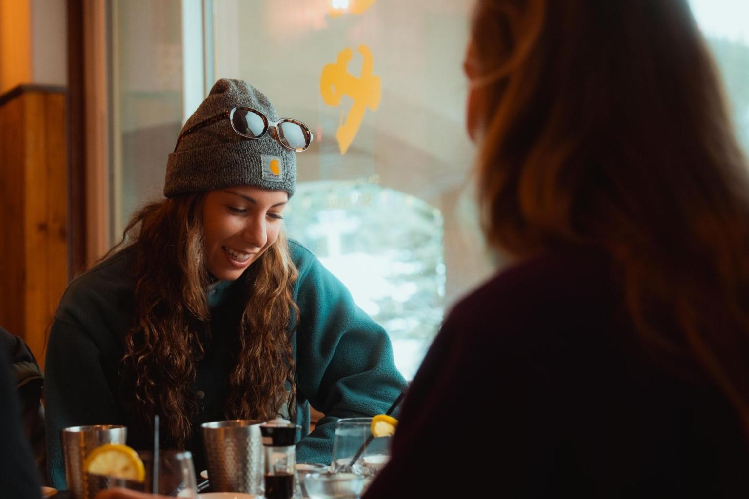 Two people chatting at a cafe table, one smiling over a cup.