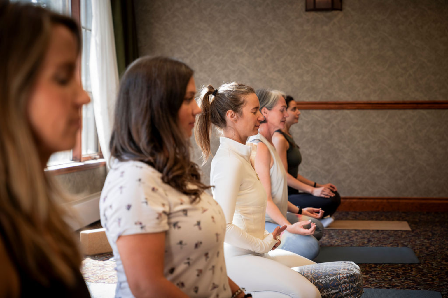 Women seated in meditation, side by side, in a room with soft lighting.