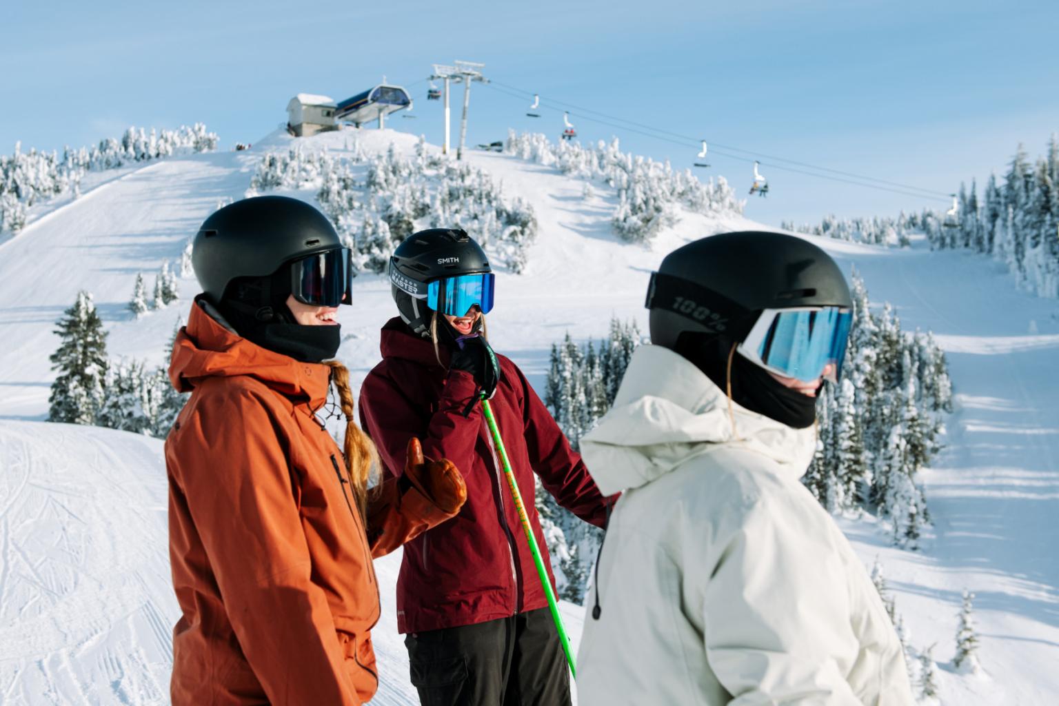 Three skiers in helmets, snowy mountain backdrop, clear sky.