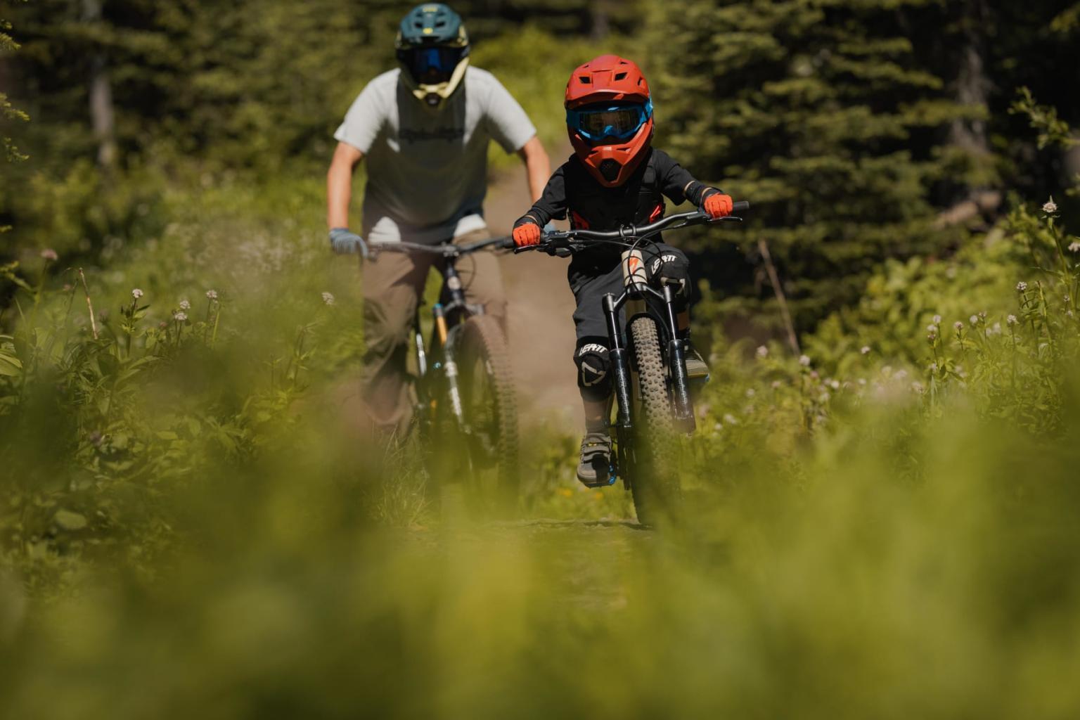 Two people mountain biking through a green forest trail.