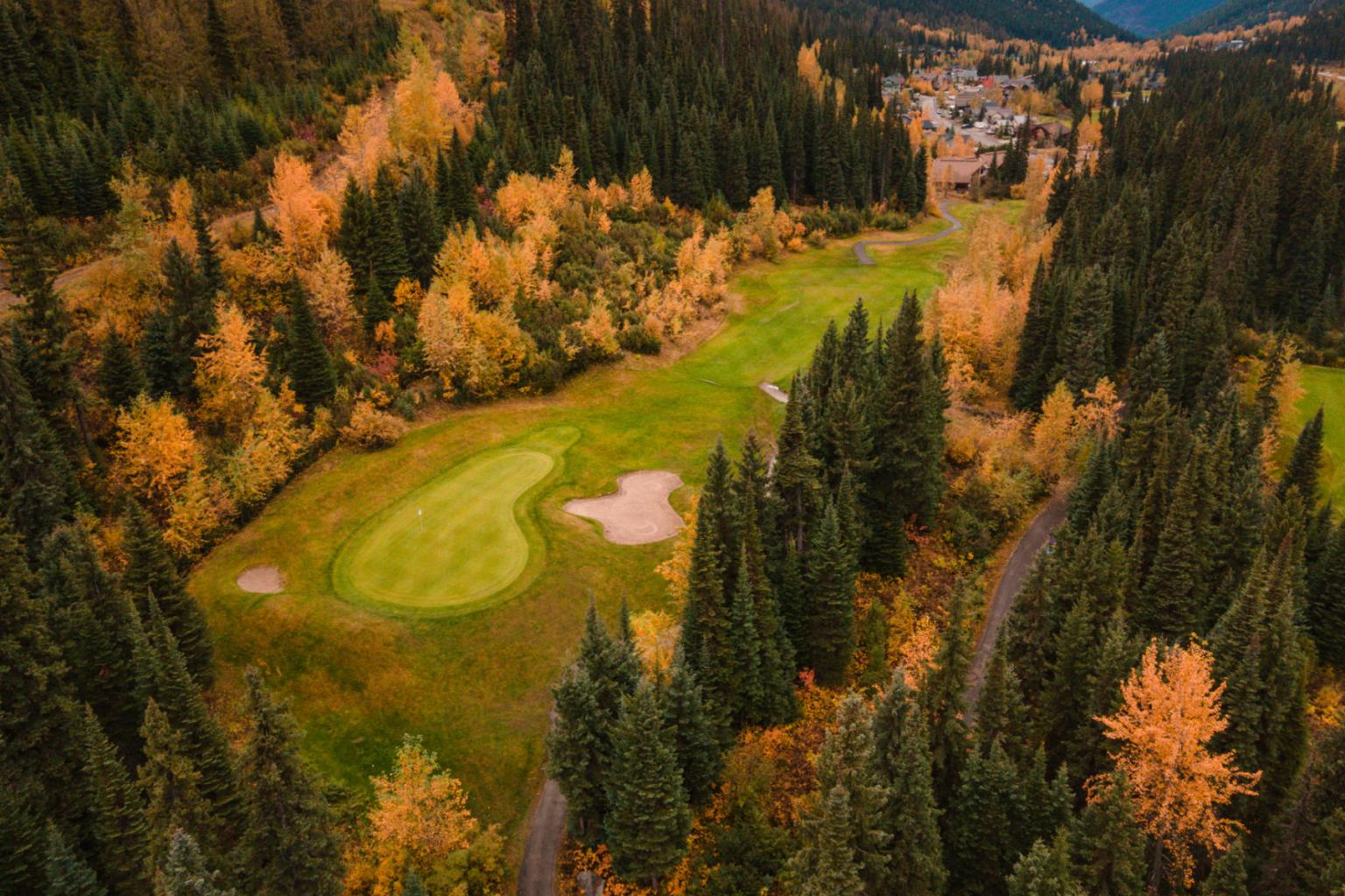 Aerial view of a golf course in autumn, surrounded by colorful trees.