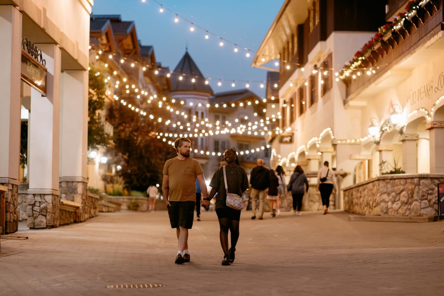 Couple walking under string lights in a lively, decorated street.