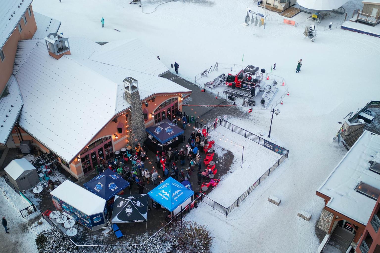Snowy village scene with people gathered near buildings and tents.