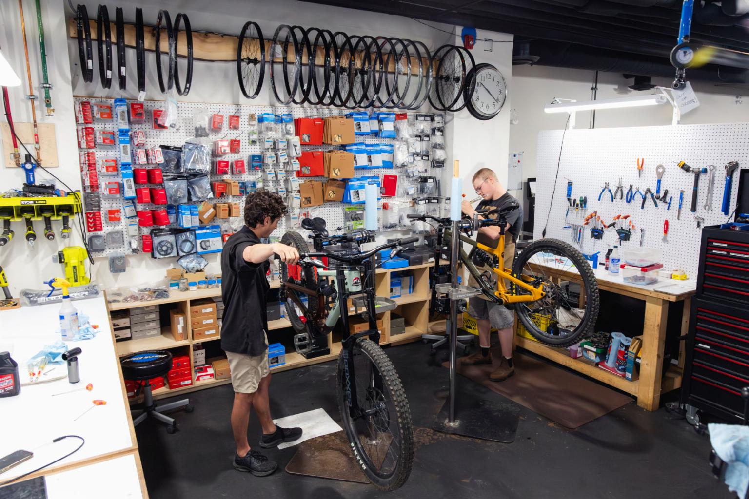 Bike mechanics working in a busy workshop, surrounded by tools and spare parts.