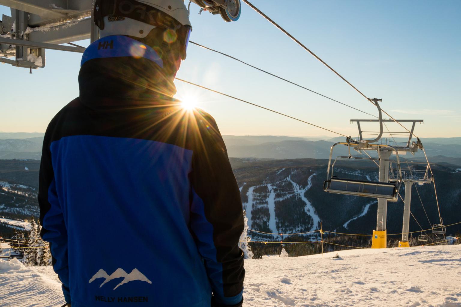Ski lift operator in a blue jacket overlooking snowy mountains at sunrise.