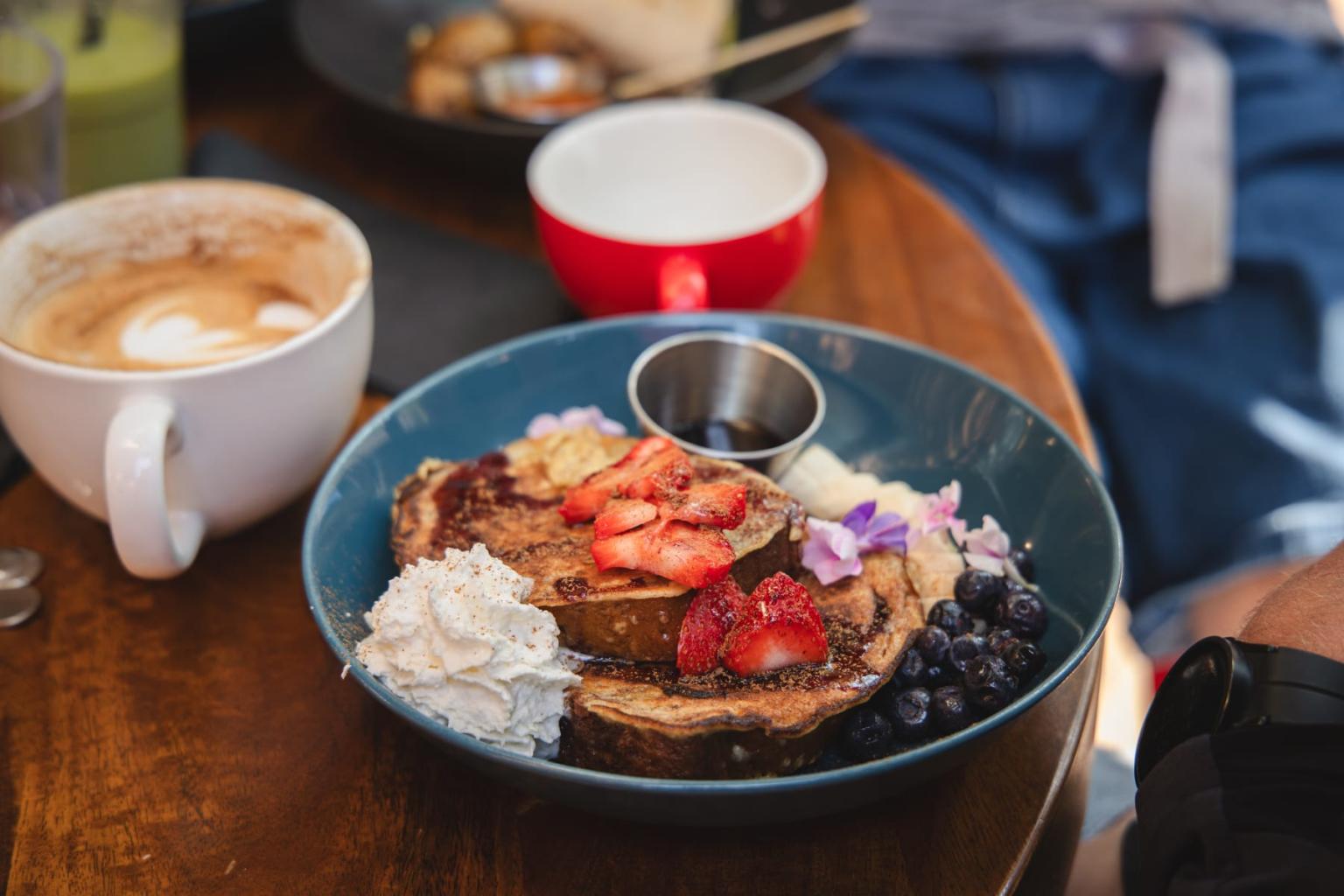 French toast with strawberries, whipped cream, and blueberries on a table with coffee.