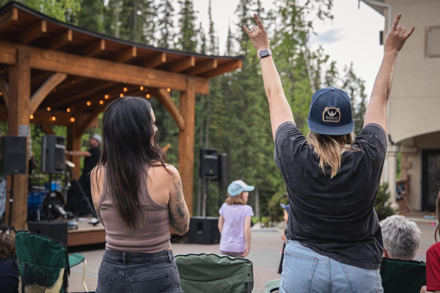 Outdoor concert with people enjoying a band on stage, surrounded by trees.