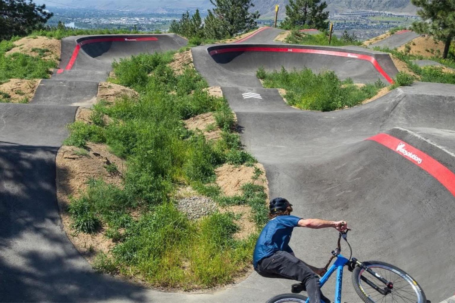 Biker on a curvy track with greenery and distant mountains.