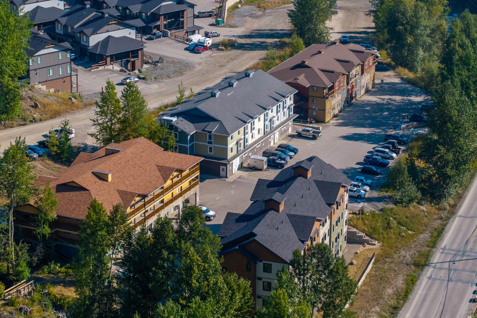 Aerial view of buildings in a wooded area with parked cars.