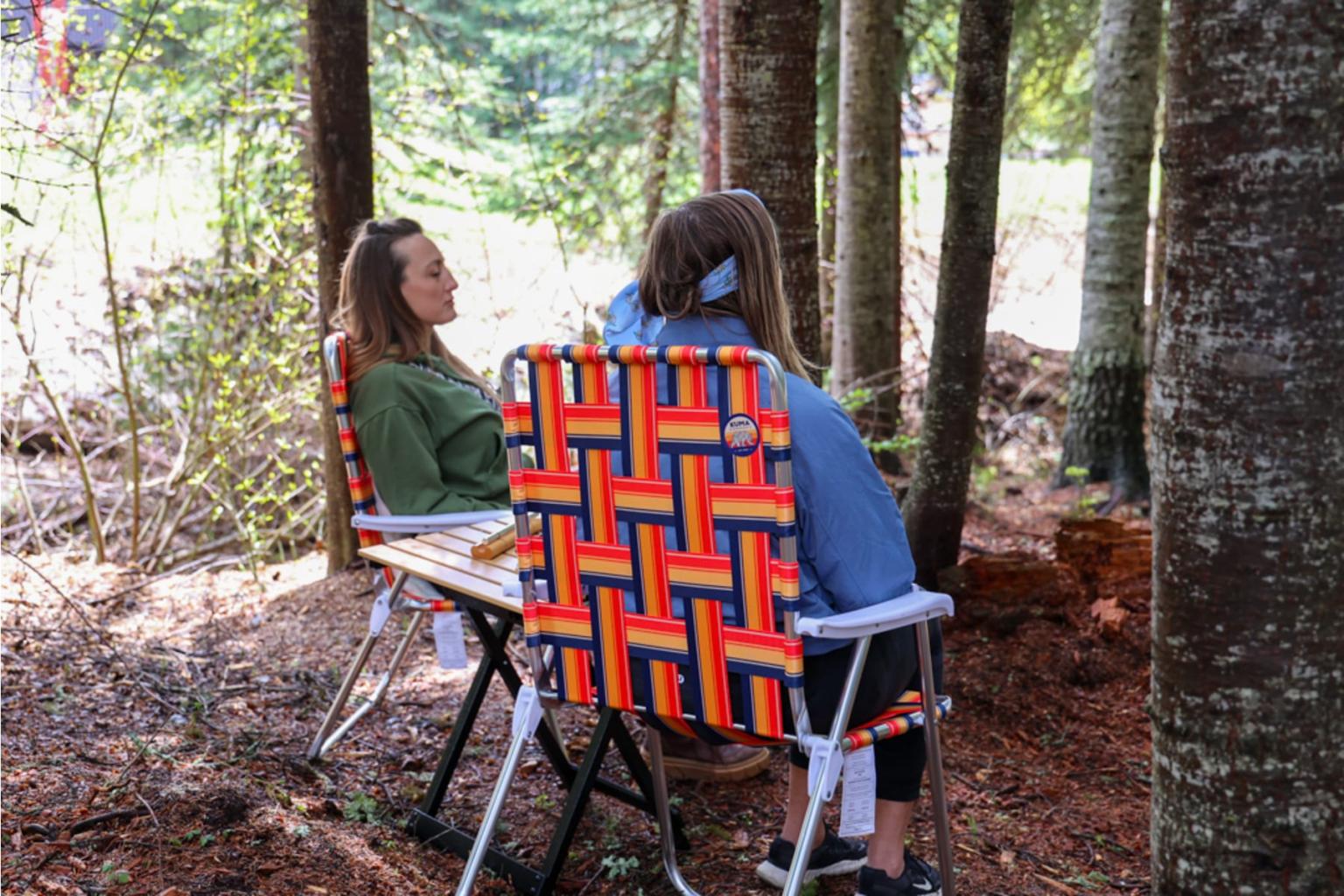 Two people sitting in colorful chairs in a forest setting.