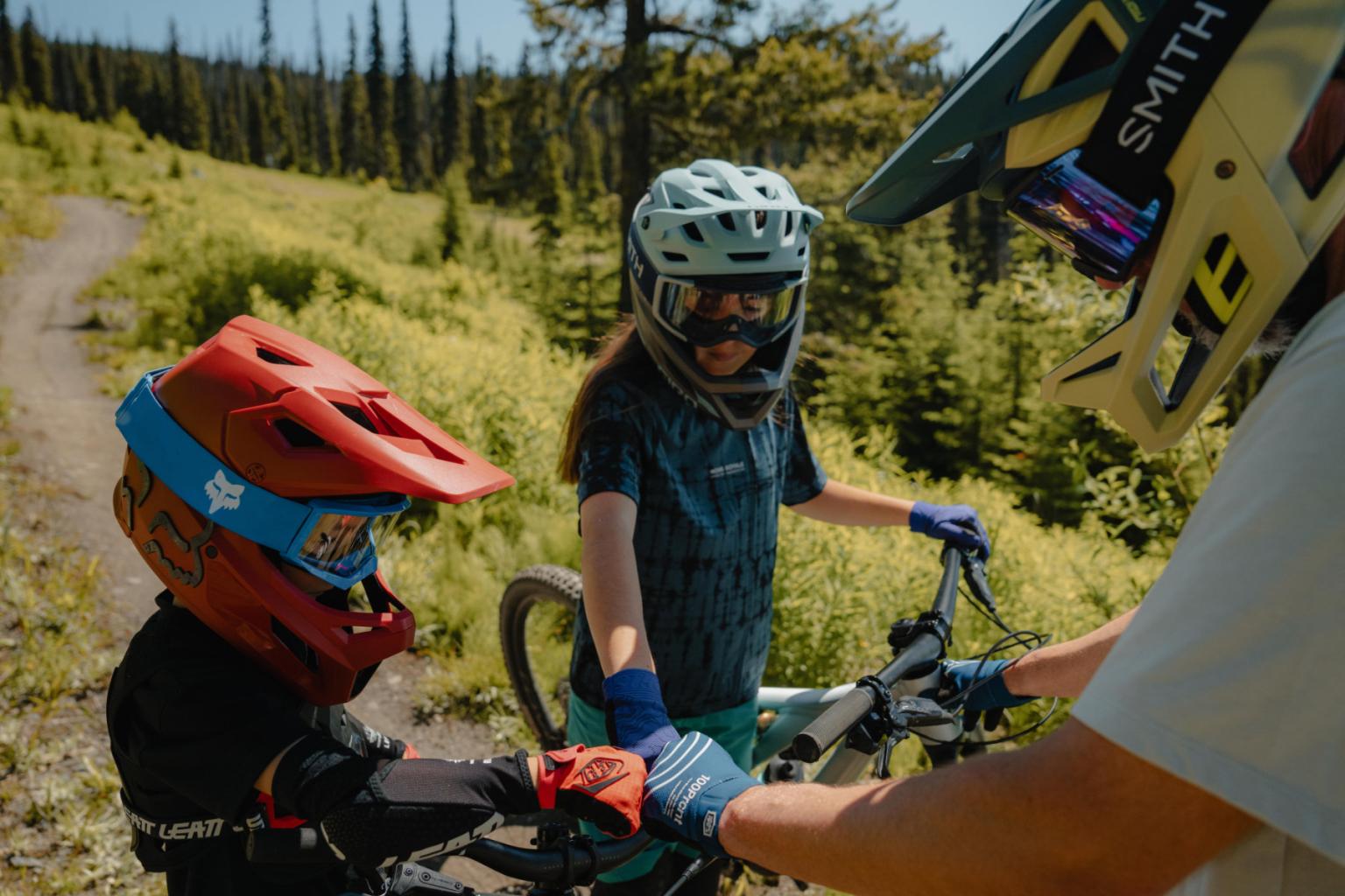 Children with helmets and bikes on a sunny forest trail.