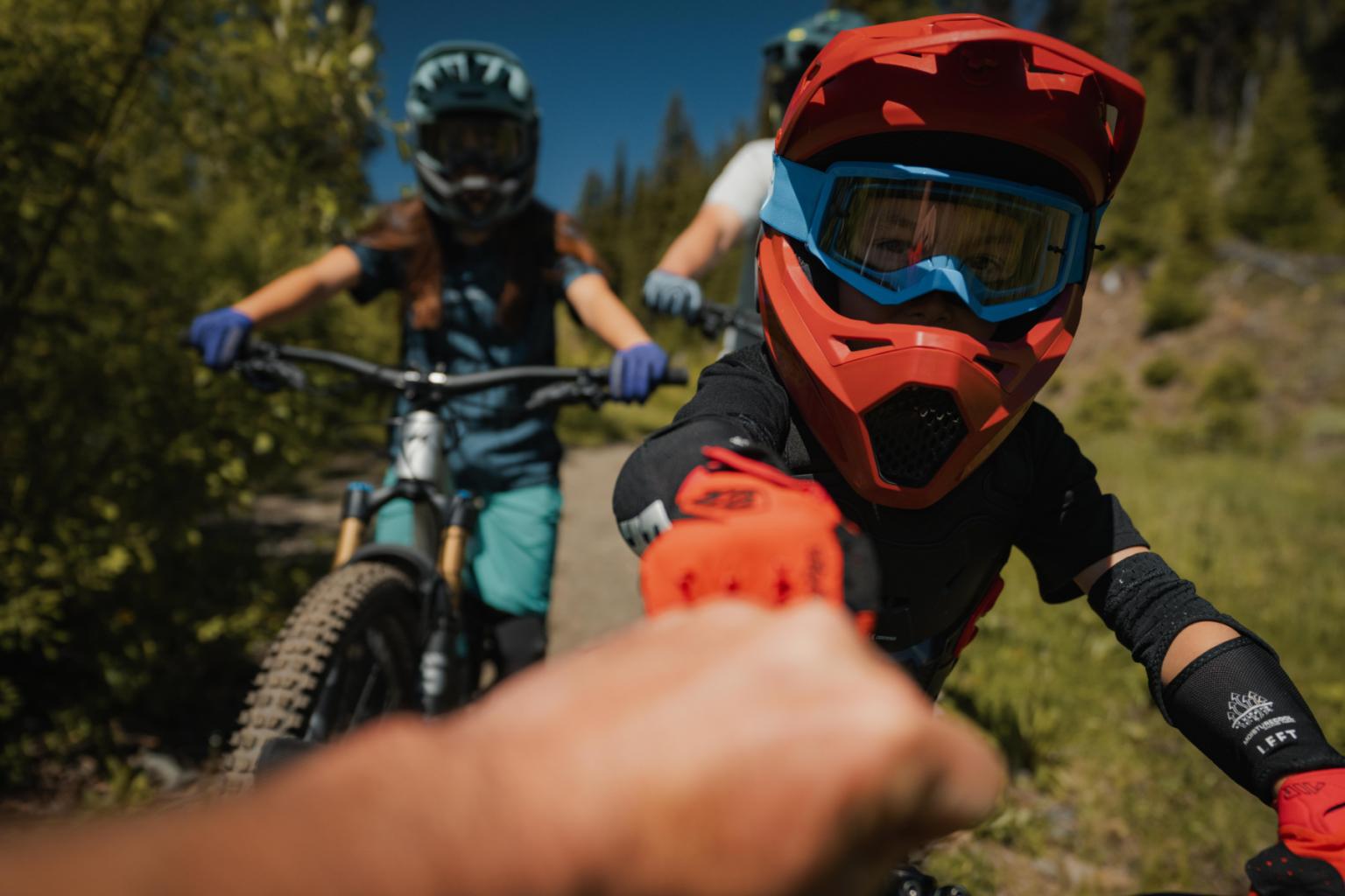 Mountain bikers fist-bumping on a trail, wearing helmets and gear.