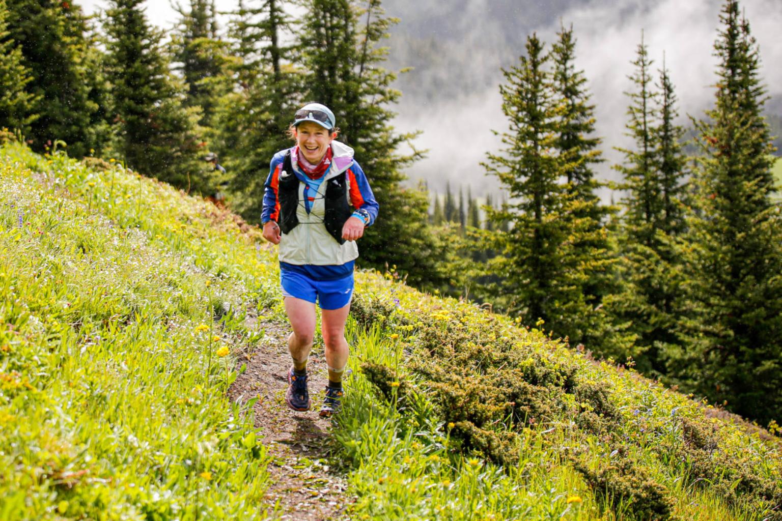 Trail runner in bright gear on a lush mountainside with evergreen trees.