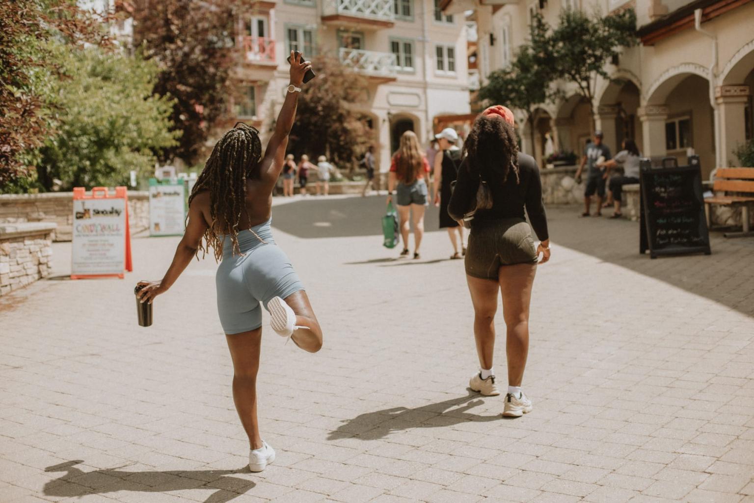 Women walking and skipping on a sunny cobblestone street with buildings in the background.